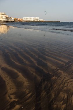 Gün batımında deniz manzarası, okyanus kıyısında ıslak sarı kumsal ve arka planda resimli bir balıkçı köyü. Playa Grande, El Medano, Tenerife, Kanarya Adaları. İspanya