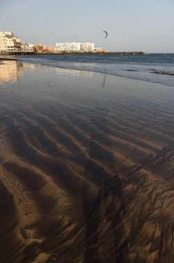 Gün batımında deniz manzarası, okyanus kıyısında ıslak sarı kumsal ve arka planda resimli bir balıkçı köyü. Playa Grande, El Medano, Tenerife, Kanarya Adaları. İspanya
