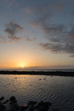 Sahilde gün batımı, altın güneş ışınları ve mavi gökyüzünde küçük bulutlar. Playa de Las Americas, Tenerife, Kanarya Adaları. İspanya