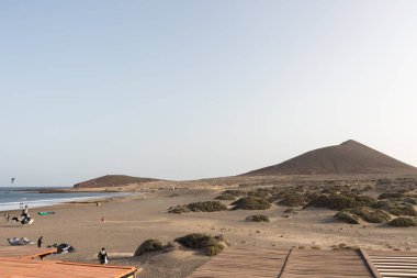 Deniz manzarası, sarı kumsal manzarası, çalılar, uçurtma sörfü yapan insanlar ve arka planda Roja dağı. Paya Grande, El Medano, Tenerife, Kanarya Adaları. İspanya