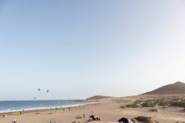 Deniz manzarası, sarı kumsal manzarası, çalılar uçurtma sörfü yapan insanlar ve arka planda Montana Roja. Paya Grande, El Medano, Tenerife, Kanarya Adaları. İspanya