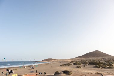 Deniz manzarası, sarı kumsal manzarası, çalılar uçurtma sörfü yapan insanlar ve arka planda Montana Roja. Paya Grande, El Medano, Tenerife, Kanarya Adaları. İspanya