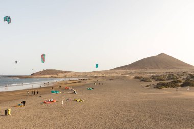 Deniz manzarası, sarı kumsal manzarası, çalılar uçurtma sörfü yapan insanlar ve arka planda Montana Roja. Paya Grande, El Medano, Tenerife, Kanarya Adaları. İspanya