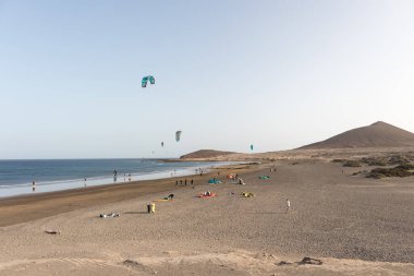 Deniz manzarası, sarı kumsal manzarası, çalılar uçurtma sörfü yapan insanlar ve arka planda Montana Roja. Paya Grande, El Medano, Tenerife, Kanarya Adaları. İspanya