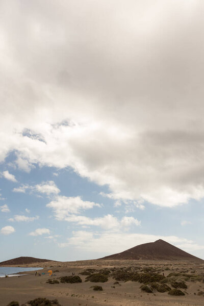 Seascape of yellow sand beach at sunset, the ocean washes the wet sand of the coast, while the sun illuminates the mountains in the background with a blue sky with large white clouds. Playa Grande, El Medano, Tenerife, Canary Islands. Spain