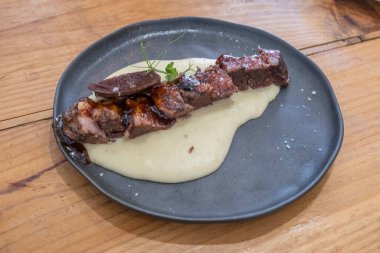  Sosu düşük sıcaklıkta pişirilmiş biftek tabağı, siyah porselen bir tabakta ve eski ahşap bir masada servis edilir.