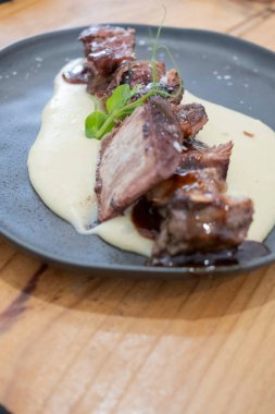  Sosu düşük sıcaklıkta pişirilmiş biftek tabağı, siyah porselen bir tabakta ve eski ahşap bir masada servis edilir.