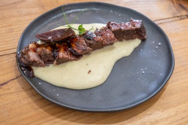  Sosu düşük sıcaklıkta pişirilmiş biftek tabağı, siyah porselen bir tabakta ve eski ahşap bir masada servis edilir.