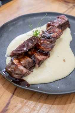  Sosu düşük sıcaklıkta pişirilmiş biftek tabağı, siyah porselen bir tabakta ve eski ahşap bir masada servis edilir.