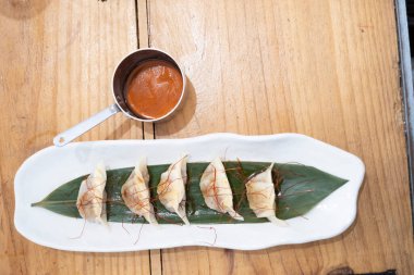 Haute mutfak tabağı, beyaz bir porselen tepside ve yeşil bir yaprak üzerinde servis edilen ağır ateşte pişirilmiş etle dolu keseler ve eski bir masanın üzerinde uzun saplı metal bir sos teknesi. Tenerife, Kanarya Adaları, İspanya