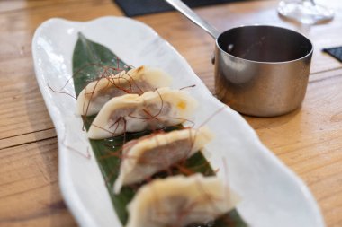 Haute mutfak tabağı, beyaz bir porselen tepside ve yeşil bir yaprak üzerinde servis edilen ağır ateşte pişirilmiş etle dolu keseler ve eski bir masanın üzerinde uzun saplı metal bir sos teknesi. Tenerife, Kanarya Adaları, İspanya