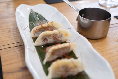 Haute mutfak tabağı, beyaz bir porselen tepside ve yeşil bir yaprak üzerinde servis edilen ağır ateşte pişirilmiş etle dolu keseler ve eski bir masanın üzerinde uzun saplı metal bir sos teknesi. Tenerife, Kanarya Adaları, İspanya