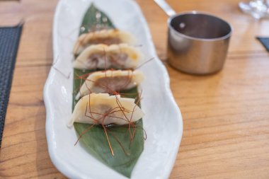 Haute mutfak tabağı, beyaz bir porselen tepside ve yeşil bir yaprak üzerinde servis edilen ağır ateşte pişirilmiş etle dolu keseler ve eski bir masanın üzerinde uzun saplı metal bir sos teknesi. Tenerife, Kanarya Adaları, İspanya