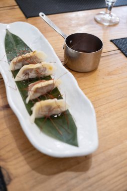 Haute mutfak tabağı, beyaz bir porselen tepside ve yeşil bir yaprak üzerinde servis edilen ağır ateşte pişirilmiş etle dolu keseler ve eski bir masanın üzerinde uzun saplı metal bir sos teknesi. Tenerife, Kanarya Adaları, İspanya