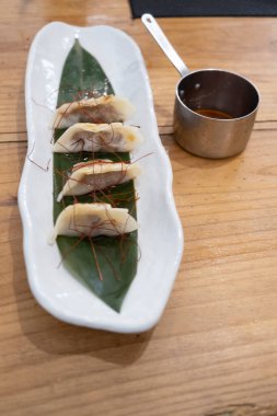 Haute mutfak tabağı, beyaz bir porselen tepside ve yeşil bir yaprak üzerinde servis edilen ağır ateşte pişirilmiş etle dolu keseler ve eski bir masanın üzerinde uzun saplı metal bir sos teknesi. Tenerife, Kanarya Adaları, İspanya