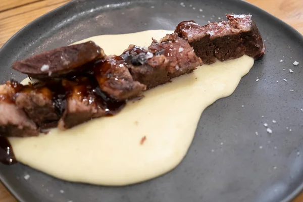  Sosu düşük sıcaklıkta pişirilmiş biftek tabağı, siyah porselen bir tabakta ve eski ahşap bir masada servis edilir.