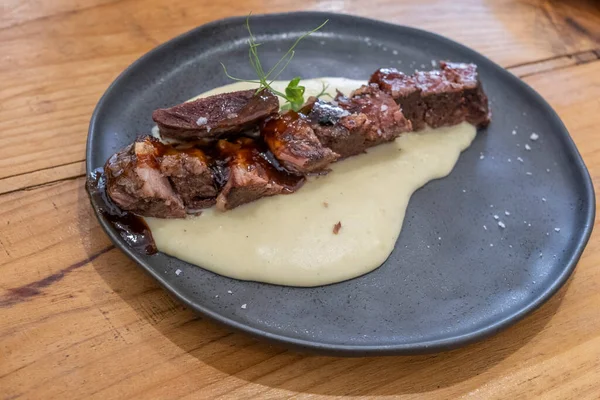  Sosu düşük sıcaklıkta pişirilmiş biftek tabağı, siyah porselen bir tabakta ve eski ahşap bir masada servis edilir.