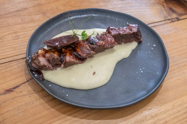  Sosu düşük sıcaklıkta pişirilmiş biftek tabağı, siyah porselen bir tabakta ve eski ahşap bir masada servis edilir.