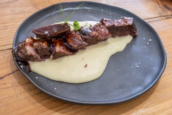 Düşük sıcaklıkta sosta pişirilmiş et kaburgalarının yakın çekimi, el yapımı siyah bir porselen tabakta ve eski bir ahşap masada servis edilir. Tenerife, Kanarya Adaları. İspanya