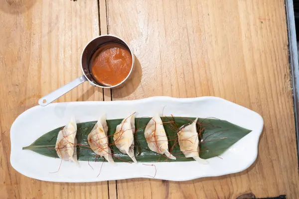 Haute mutfak tabağı, beyaz bir porselen tepside ve yeşil bir yaprak üzerinde servis edilen ağır ateşte pişirilmiş etle dolu keseler ve eski bir masanın üzerinde uzun saplı metal bir sos teknesi. Tenerife, Kanarya Adaları, İspanya