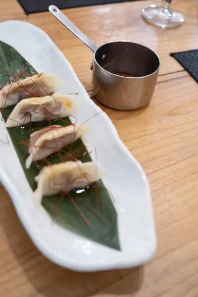 stock image Haute cuisine dish, sachets filled with braised meat served on a white porcelain tray and on a green leaf, and with a small metal sauce boat with a long handle, on a vintage table. Tenerife, Canary Islands, Spain