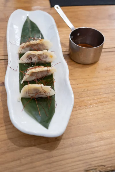 Haute mutfak tabağı, beyaz bir porselen tepside ve yeşil bir yaprak üzerinde servis edilen ağır ateşte pişirilmiş etle dolu keseler ve eski bir masanın üzerinde uzun saplı metal bir sos teknesi. Tenerife, Kanarya Adaları, İspanya