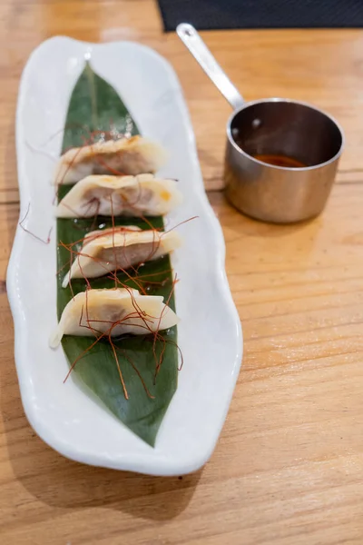 Haute mutfak tabağı, beyaz bir porselen tepside ve yeşil bir yaprak üzerinde servis edilen ağır ateşte pişirilmiş etle dolu keseler ve eski bir masanın üzerinde uzun saplı metal bir sos teknesi. Tenerife, Kanarya Adaları, İspanya