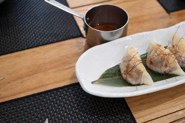 Haute mutfak tabağı, beyaz bir porselen tepside ve yeşil bir yaprak üzerinde servis edilen ağır ateşte pişirilmiş etle dolu keseler ve eski bir masanın üzerinde uzun saplı metal bir sos teknesi. Tenerife, Kanarya Adaları, İspanya