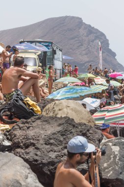 TENERİFE, SPAIN 11 - AGUSTAN 2013: Bir grup insan günü plajda şemsiyelerle, mayolarıyla, güneşlenerek, sahilde yüzerek ve kıyıdan badiba şampiyonasını izleyerek geçiriyorlar. Tenerife, Kanarya Adaları, Sp