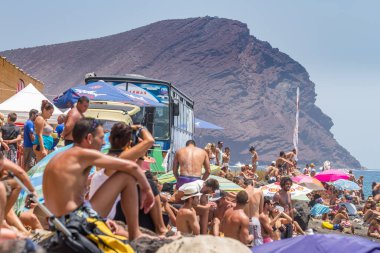 TENERİFE, SPAIN 11 - AGUSTAN 2013: Bir grup insan günü plajda şemsiyelerle, mayolarıyla, güneşlenerek, sahilde yüzerek ve kıyıdan badiba şampiyonasını izleyerek geçiriyorlar. Tenerife, Kanarya Adaları, Sp