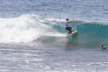 TENERIFE, SPAIN 11 - HAZİRAN 2013: Erkekler vücut tahtası şampiyonasında yarışan bir çocuğun dalgada dizlerinin üzerinde sörf yaparken farklı ve inanılmaz manevralar ve dönüşler yaparak bir sürü köpük oluşturduğu açık çekim. Tenerife, Kanarya Adaları, İspanya
