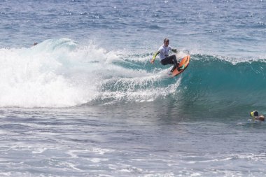 TENERIFE, SPAIN 11 - HAZİRAN 2013: Erkekler vücut tahtası şampiyonasında yarışan bir çocuğun dalgada dizlerinin üzerinde sörf yaparken farklı ve inanılmaz manevralar ve dönüşler yaparak bir sürü köpük oluşturduğu açık çekim. Tenerife, Kanarya Adaları, İspanya