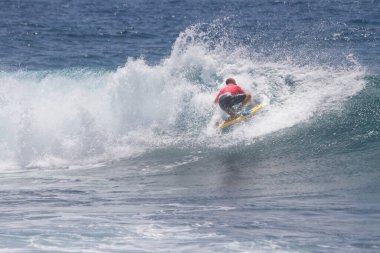 TENERIFE, SPAIN 11 - HAZİRAN 2013: Erkekler vücut tahtası şampiyonasında yarışan bir çocuğun dalgada dizlerinin üzerinde sörf yaparken farklı ve inanılmaz manevralar ve dönüşler yaparak bir sürü köpük oluşturduğu açık çekim. Tenerife, Kanarya Adaları, İspanya