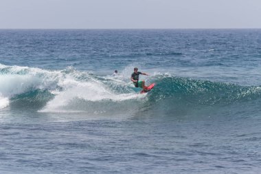 TENERIFE, SPAIN 11 - HAZİRAN 2013: Erkekler vücut tahtası şampiyonasında yarışan bir çocuğun dalgada dizlerinin üzerinde sörf yaparken farklı ve inanılmaz manevralar ve dönüşler yaparak bir sürü köpük oluşturduğu açık çekim. Tenerife, Kanarya Adaları, İspanya