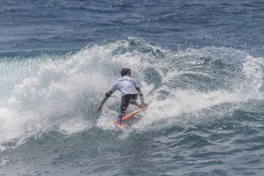 TENERIFE, SPAIN 11 - HAZİRAN 2013: Erkekler vücut tahtası şampiyonasında yarışan bir çocuğun dalgada dizlerinin üzerinde sörf yaparken farklı ve inanılmaz manevralar ve dönüşler yaparak bir sürü köpük oluşturduğu açık çekim. Tenerife, Kanarya Adaları, Spai