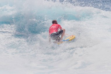 TENERIFE, SPAIN 11 - HAZİRAN 2013: Erkekler vücut tahtası şampiyonasında yarışan bir çocuğun dalgada dizlerinin üzerinde sörf yaparken farklı ve inanılmaz manevralar ve dönüşler yaparak bir sürü köpük oluşturduğu açık çekim. Tenerife, Kanarya Adaları, Spai