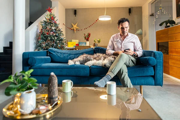 Adam Oturma Odasındaki Koltukta Bağdaş Kurup Köpeğiyle Noel Süslemeleri Yaparken — Stok fotoğraf