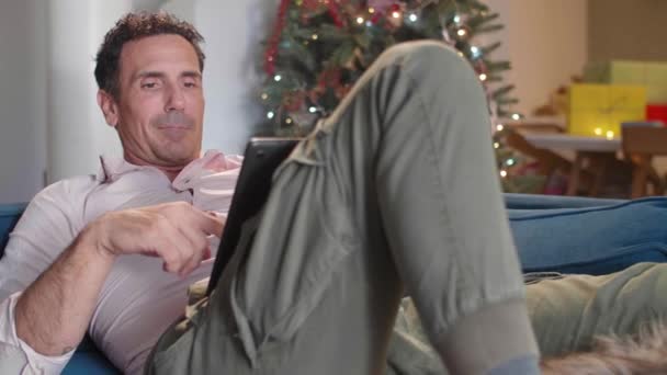 Adam Oturma Odasındaki Kanepede Oturuyor Noel Süsleriyle Köpeğini Okşuyor Tablet — Stok video