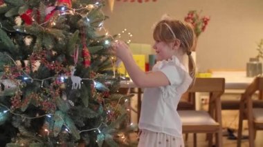 Oturma odasındaki Noel ağacını süsleyen küçük kız aynı zamanda Noel ruhu ve gelecek Noel 'le süslenmiş..
