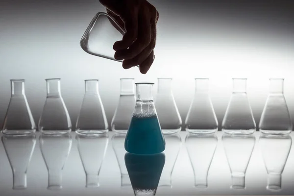科学実験室のガラスのエルレンマイヤーのフラスコに白い液体を反射面にガラス器具で注ぐ手 — ストック写真
