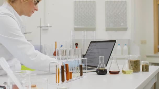 化学科学家在实验室与大麻Cbd和Cbda油一起工作 她正在用笔记本电脑 用玻璃管和消声器瓶写下结果 大麻籽保健药品 — 图库视频影像