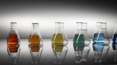Boş ve karışık renkli sıvı Erlenmeyer şişeleri masaya yansıyor.