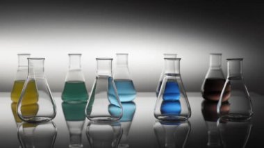 Boş ve karışık renkli sıvı Erlenmeyer şişeleri masaya yansıyor.