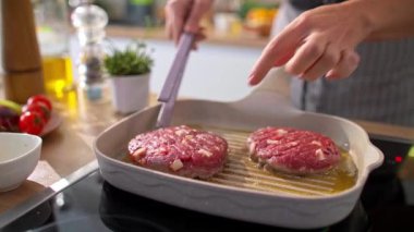 Mutfaktaki ızgara tavada hamburger pişirirken, şefin nazikçe hamburgeri çevirmesi ve hazır olup olmadığını kontrol etmesi..
