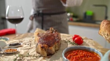 Bifteğin ahşap bir mutfak tahtasında servis edildiği yakın plan bir manzara, yan taraflarda ise sebze ve baharatlar gibi küçük kaseler var..