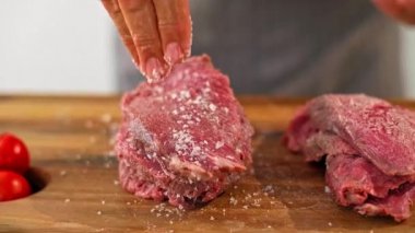 Pişirme aşamasında şefin ellerine baharat eklemek için yakın çekim. Çalışma yüzeyinde çeşitli küçük mutfak kaseleri ve sebzeler görülebilir..