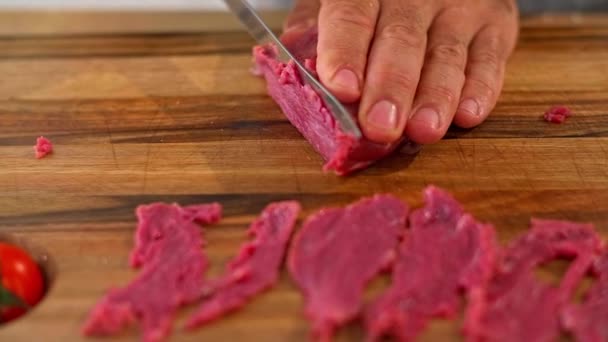 木製のキッチンボード上の準備段階で シェフの手を細かく切ったカルパッチョ肉のクローズアップ 作業面には様々な小鉢や野菜を見ることができます — ストック動画
