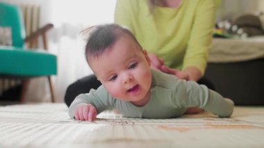 Anne oturma odasında bebekle egzersiz yapıyor, karnının üzerinde yuvarlanmasına yardım ediyor..