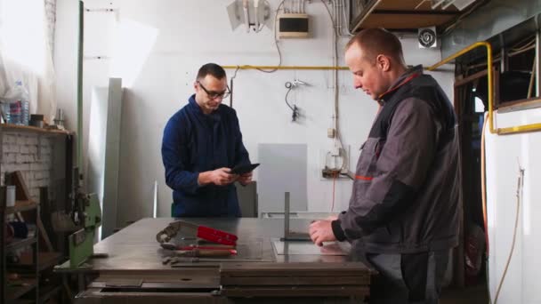一位铁匠和他的同事工程师同事正在他们的车间里一起工作 而工程师则在使用平板电脑 — 图库视频影像