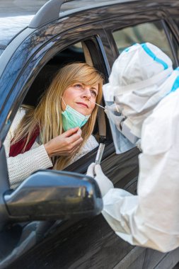 Otomobil sürücüsü COVID-19 testi yapıyor. Kadın hastadan araba camından geniz örneği alıyor. Coronavirus için PCR testi yapıyor..